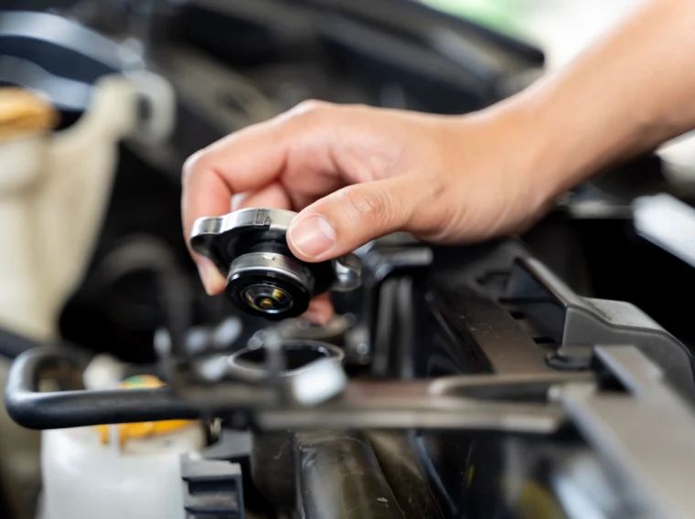 A person is holding a radiator cap of a car.