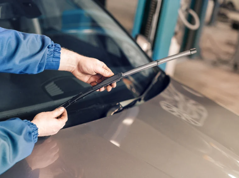 A person in a blue jacket replaces a windshield wiper blade on a car, demonstrating expert Windshield Wiper Blade services.