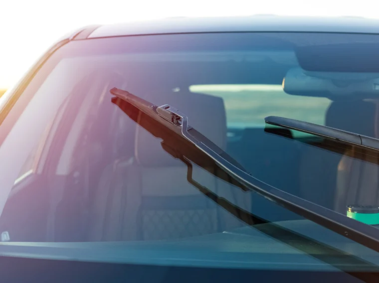 Close-up view of a car windshield with one wiper raised, showing the interior in the background—perfect for illustrating wiper replacement or wiper blade replacement services.