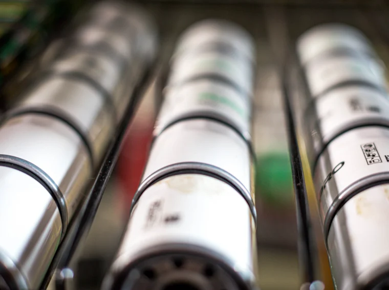 Close-up view of cylindrical metal objects, possibly batteries or industrial components, arranged in parallel rows on a metal rack.