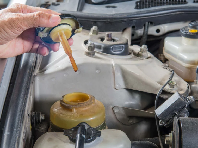 A hand is checking the brake fluid level in a car by inspecting the fluid on the dipstick attached to the brake fluid reservoir cap, an important step before performing a Power Steering Service or a Steering Fluid Flush.