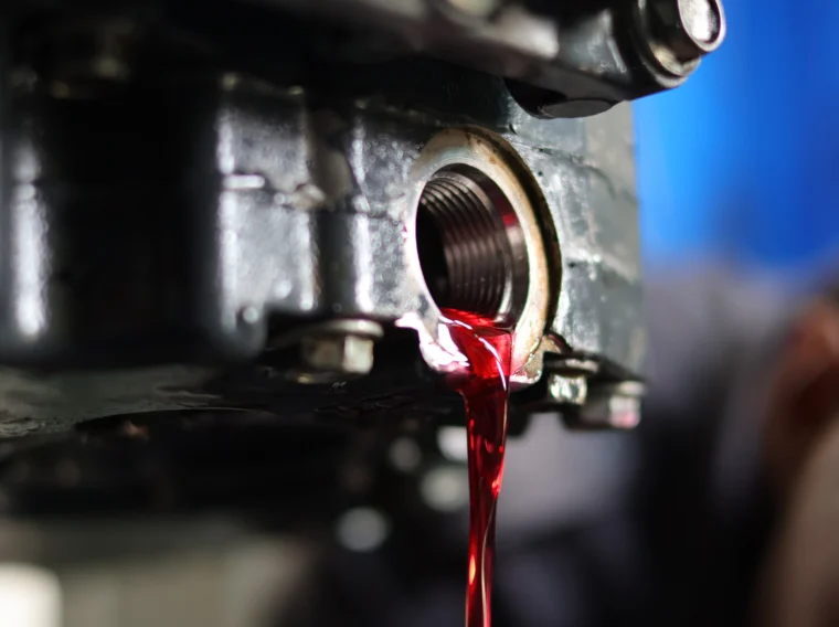 Red transmission fluid flowing out of a metal engine component during a maintenance procedure.