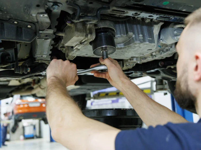 A mechanic uses a wrench to work on the underside of a lifted vehicle in an auto repair shop.