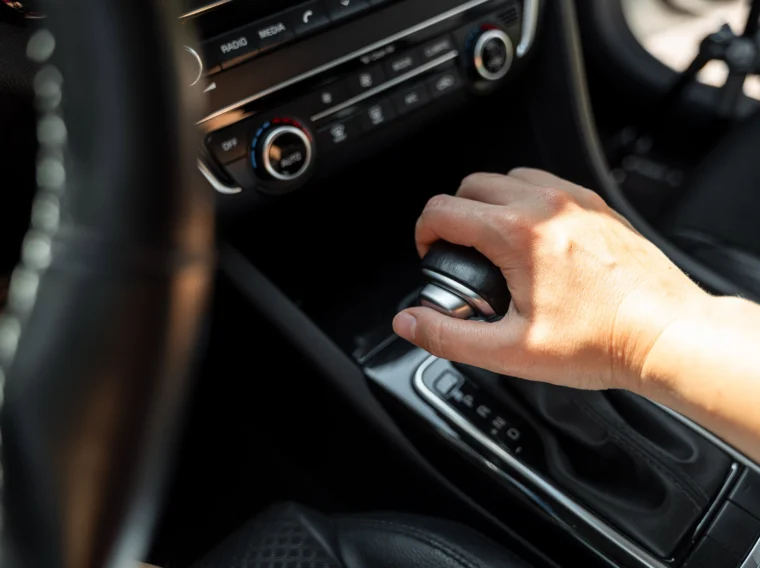 A person’s hand is gripping the gear shift lever in the center console of a car interior.