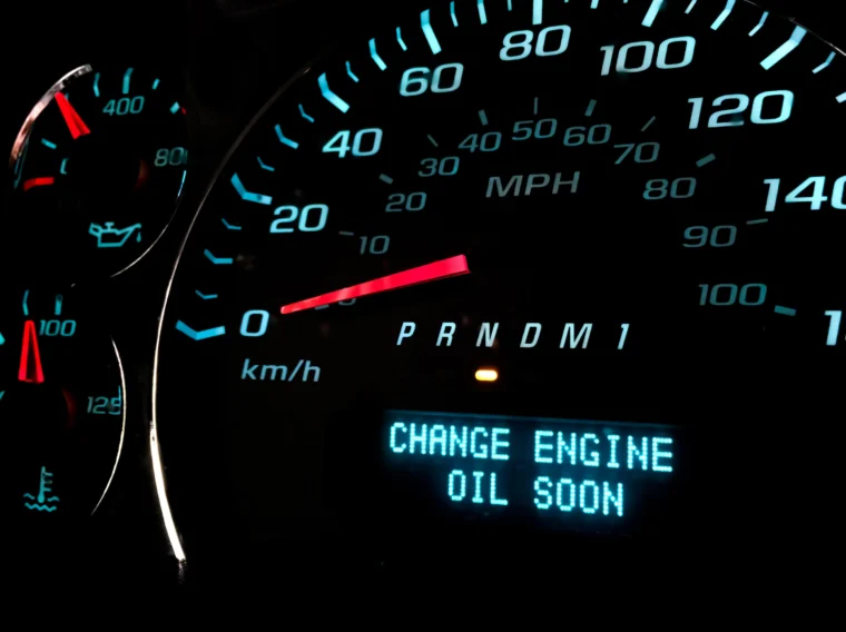 Close-up of a car dashboard showing the speedometer, fuel and temperature gauges, and a warning message reading "CHANGE ENGINE OIL SOON.