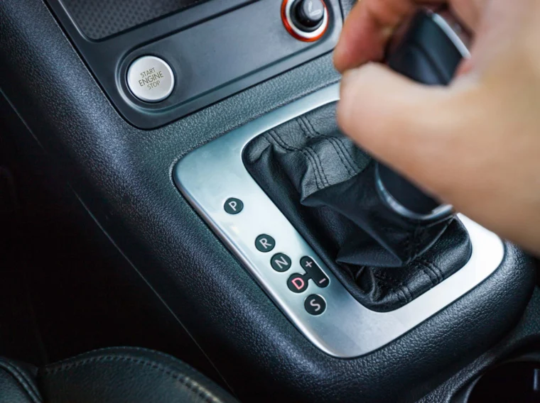 A hand shifting the gear lever of an automatic transmission, with gear positions P, R, N, D, and manual (+/-) modes visible—highlighting the importance of regular Transmission Services for smooth operation.