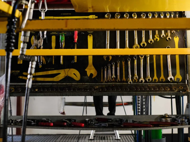 A pegboard displays various wrenches and hand tools neatly organized, with lower shelves holding additional tools in a workshop setting specializing in Engine Services.