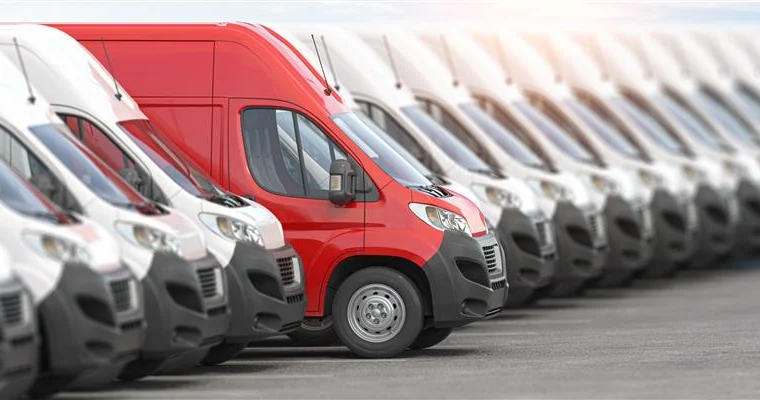 A row of white vans from a Fleet Program is parked in a lot, with one red van standing out in the center.