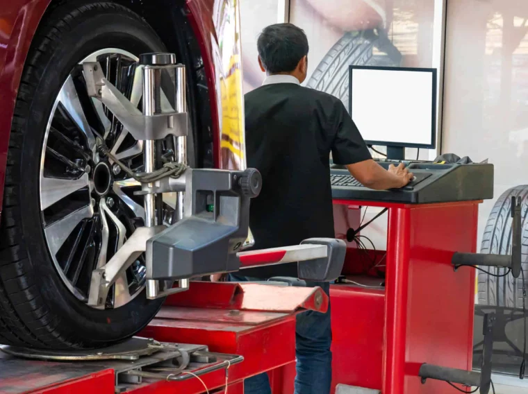 A mechanic stands at a computer workstation while performing a wheel alignment, an essential part of car maintenance, on a car mounted on a lift.