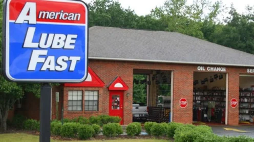 A brick auto service building with two garage bays, a red entrance, and a sign reading "American Lube Fast" in front.