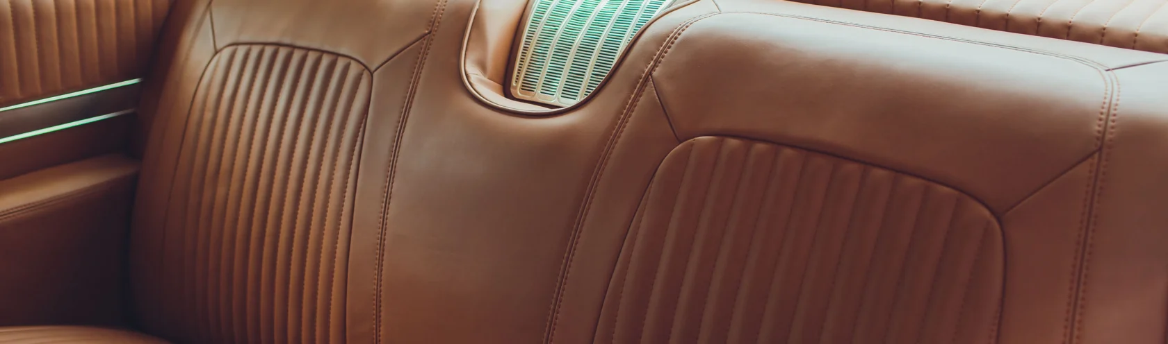 Close-up of the brown leather backseat of a vintage car, featuring vertical stitching and a chrome air vent—classic details that define Cars of Character.