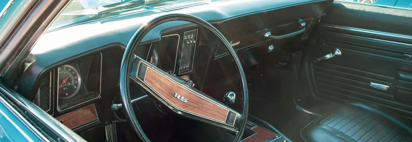 Interior view of a vintage Cars of Character, featuring a wooden RS-branded steering wheel, black leather seats, and classic dashboard controls.