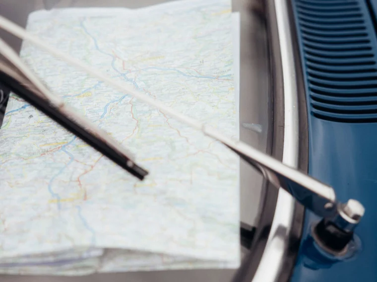 A folded paper map is held under a windshield wiper on the hood of a blue car, showcasing one of those classic Cars of Character.
