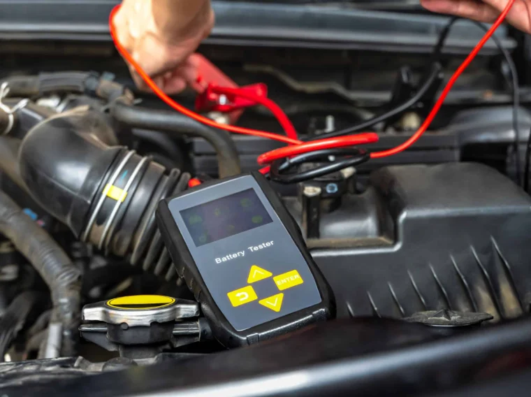 A battery tester connected to a car engine with red and black cables while a person adjusts the connections, demonstrating professional Battery Services.